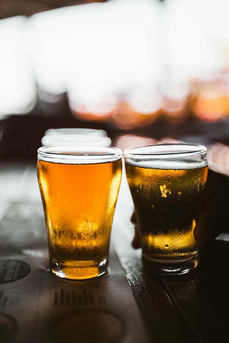 Glasses of cold beer sweating from the heat sitting on a wooden table